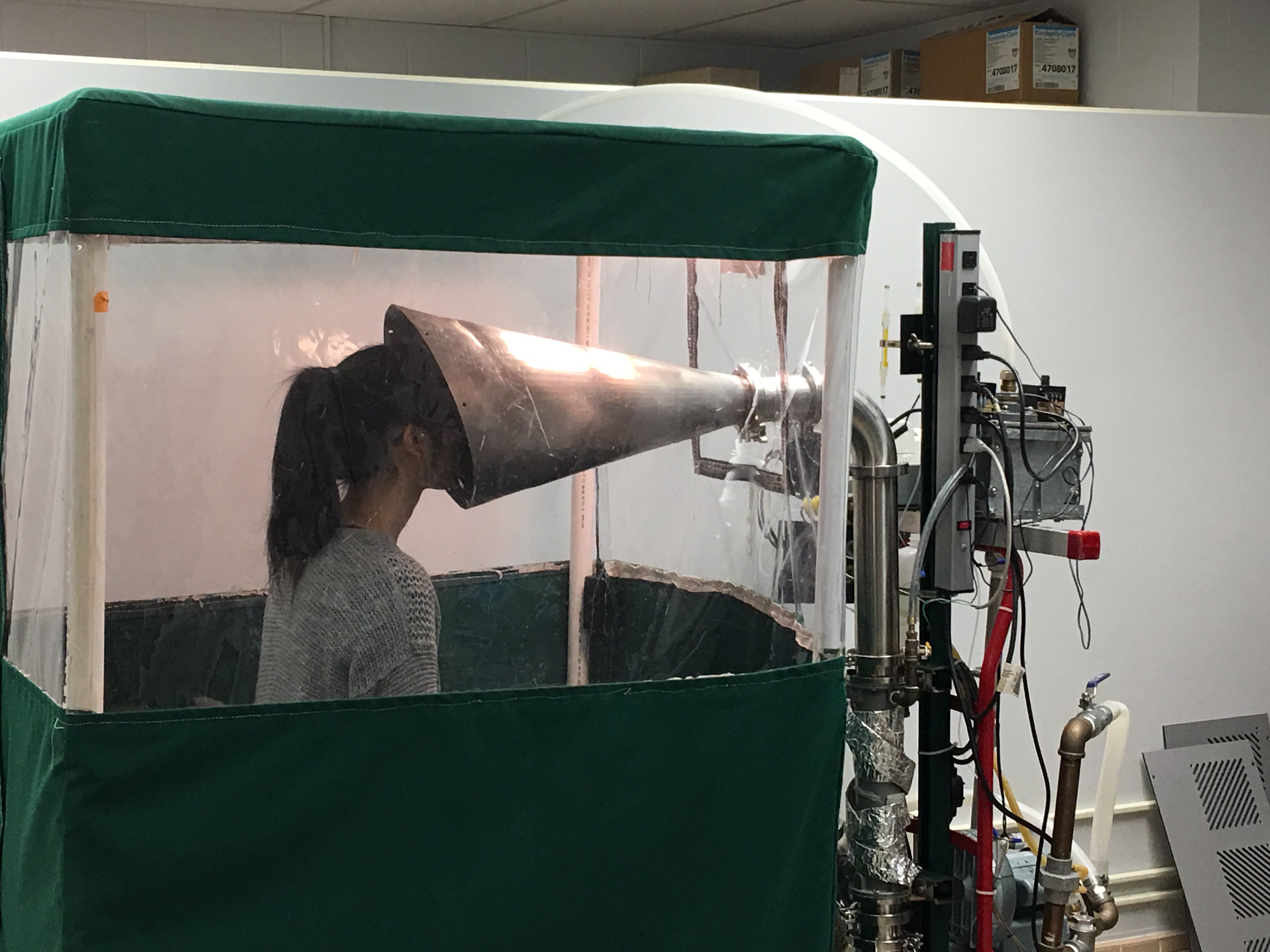 person breathing into device that looks like an old-fashioned loudspeaker, encased in a green tent with a clear plastic window person breathing into device that looks like an old-fashioned loudspeaker, encased in a green tent with a clear plastic window