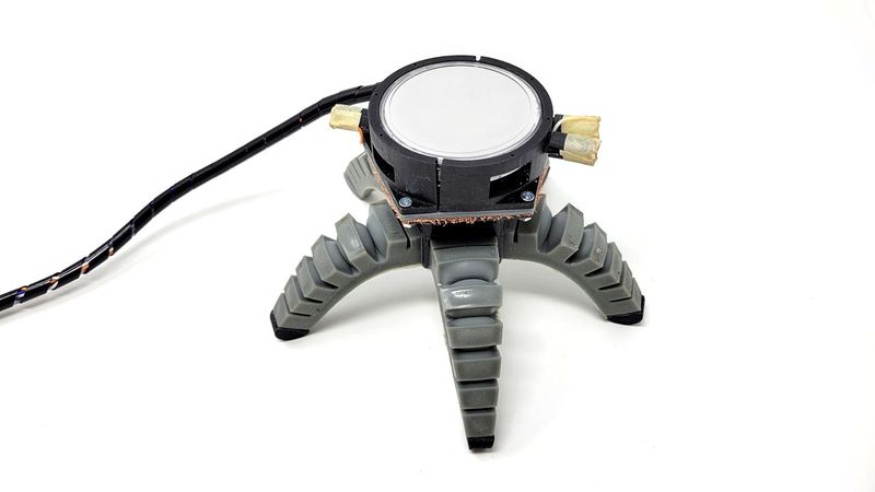 spider-like soft robot with five legs, with a large round sensor on the top and a black wire trailing from it