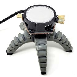 spider-like soft robot with five legs, with a large round sensor on the top and a black wire trailing from it