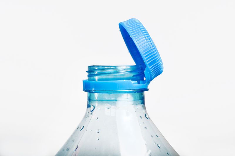 Close up of new cap attached to plastic bottle, connected to the neck of the bottle by solid tab attached to safety ring.