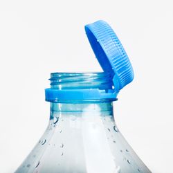 Close up of new cap attached to plastic bottle, connected to the neck of the bottle by solid tab attached to safety ring.