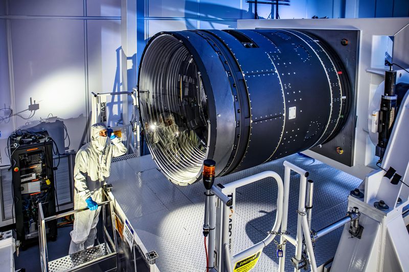 LSST Camera Deputy Project Manager Travis Lange shines a flashlight into the LSST Camera. The camera is a black cylinder much bigger than him 