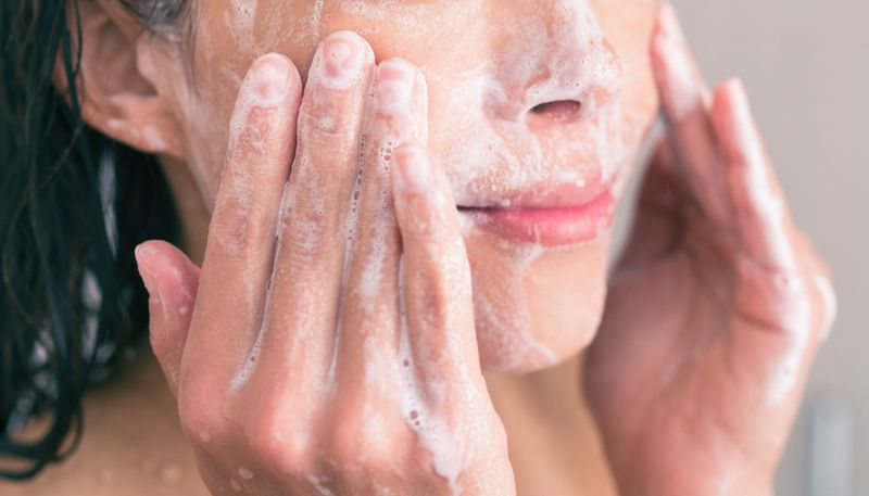 Woman rubbing bubbles of cleanser into her face with her hands.