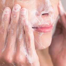 Woman rubbing bubbles of cleanser into her face with her hands.