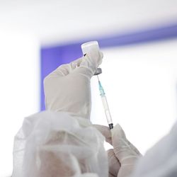 medical professional in green surgical mask, gown, face shield and gloves draws up vaccine into syringe