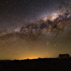 A night view. A windmill and a house are seen as silhouttes. IN the sky the milky way dominates the whole sky.