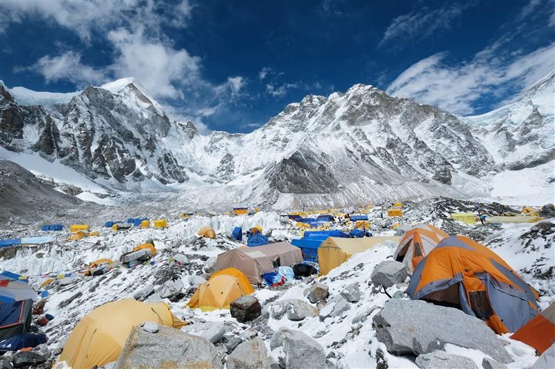 A photo of the tents camped out at the Everest Base Camp. The tents are scatted around a snow covered and abundantly rocky space situated in what looks like a bowl surrounded by mountains.  