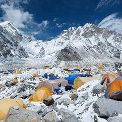 A photo of the tents camped out at the Everest Base Camp. The tents are scatted around a snow covered and abundantly rocky space situated in what looks like a bowl surrounded by mountains.  
