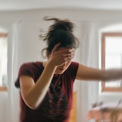 woman covering eyes and leaning on doorframe, with backdrop blurred to indicate dizziness