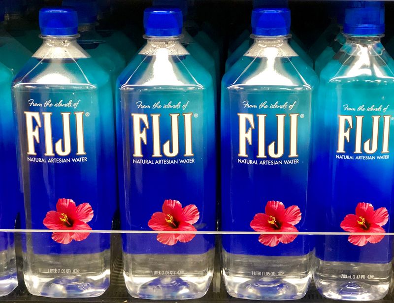 four bottles of Fiji mineral water, which have blue caps and labels with white text and a pink flower, sitting on a store shelf