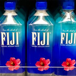 four bottles of Fiji mineral water, which have blue caps and labels with white text and a pink flower, sitting on a store shelf