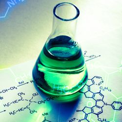 Conical flask filled with green liquid on top of a sheet of paper with chemical reactions written on