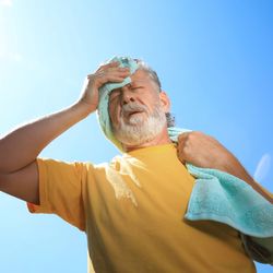 Senior man with towel suffering from heat stroke outdoors, low angle view