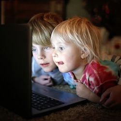 two kids watching a something on a laptop together