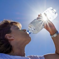 Woman, senior, drinking water in the sunlight, back lit image with sunbeams. 