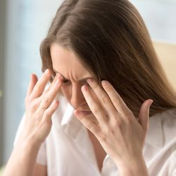 Woman wearing white shirt pressing her fingers around her eyes as though in pain.