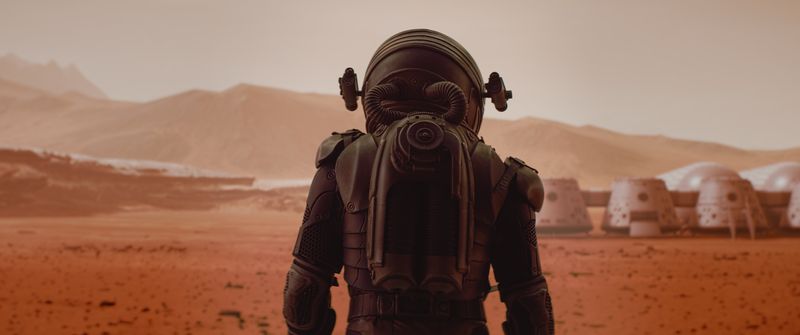 Back view of astronaut wearing space suit walking on a surface of a red planet. Martian base and rover in the background. 