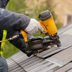 worker on a roof wearing high-vis jacket and gloves operating a yellow pneumatic nail gun