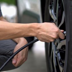 Person in jeans and blue T-shirt crouching down, holding a black rubber hose attached to a car tire