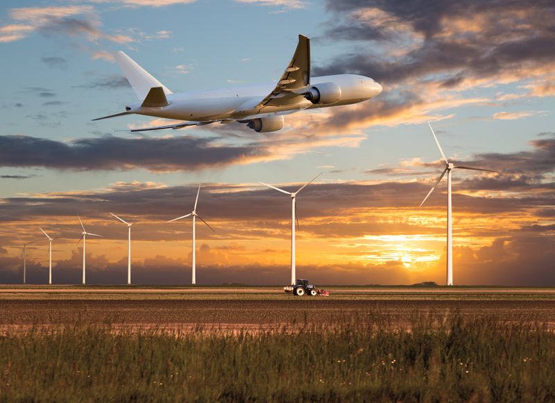 Plane takes off above a farm field and wind electric generators