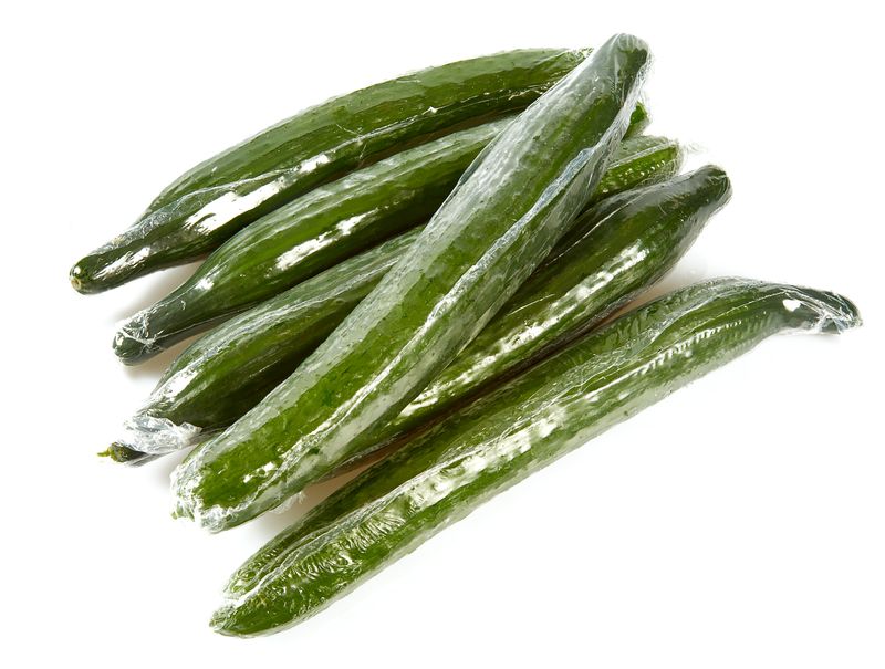 Six cucumbers wrapped in plastic on a white background