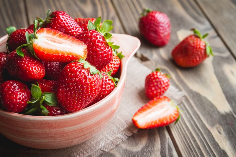 Fresh strawberries in a bowl on wooden table.