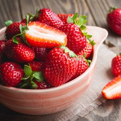 Fresh strawberries in a bowl on wooden table.