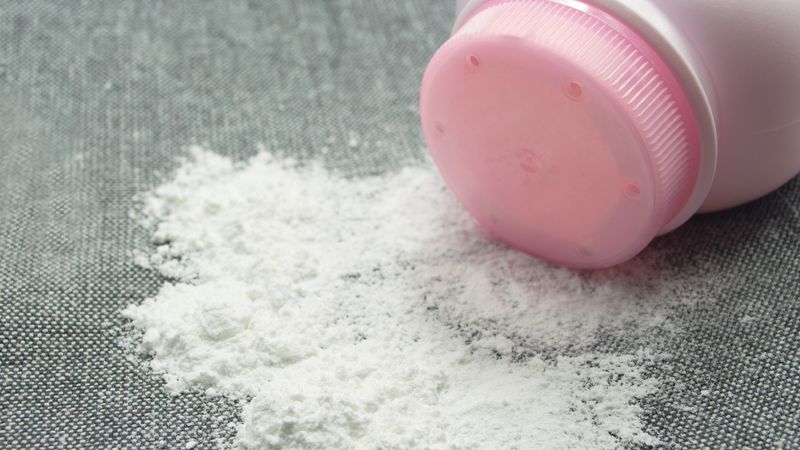 close-up of talcum powder spilling out from a pink bottle onto a grey fabric surface