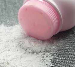 close-up of talcum powder spilling out from a pink bottle onto a grey fabric surface