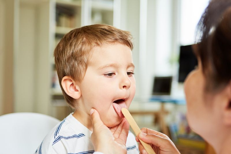 doctor examining young boy using tongue suppressor