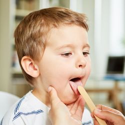 doctor examining young boy using tongue suppressor