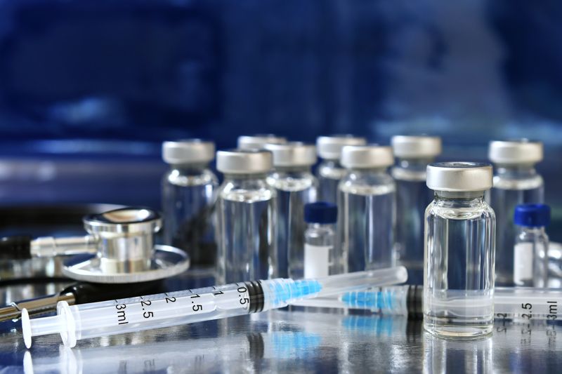 vaccine vials on a table with two syringes in the foreground and a stethoscope 