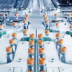 production line with lots of medical vials with orange lids on a conveyor belt