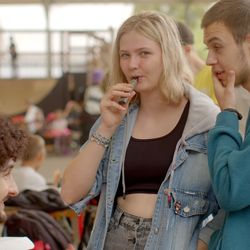 Photo of three young people, girl in the middle is holding a vape up to her mouth while the two boys either side of her are chatting