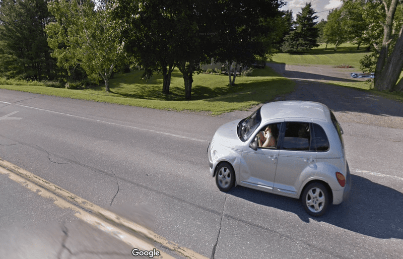 A screenshot of Google Street View showing silver car driving on the road. 