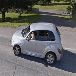 A screenshot of Google Street View showing silver car driving on the road. 