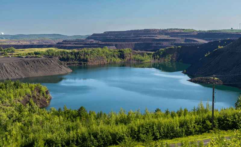 An iron mine industrial area area looks a blue lake and green forest in Minnesota.