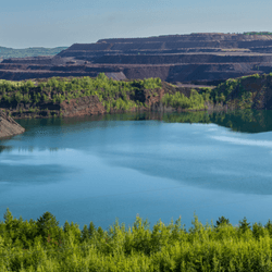 An iron mine industrial area area looks a blue lake and green forest in Minnesota.