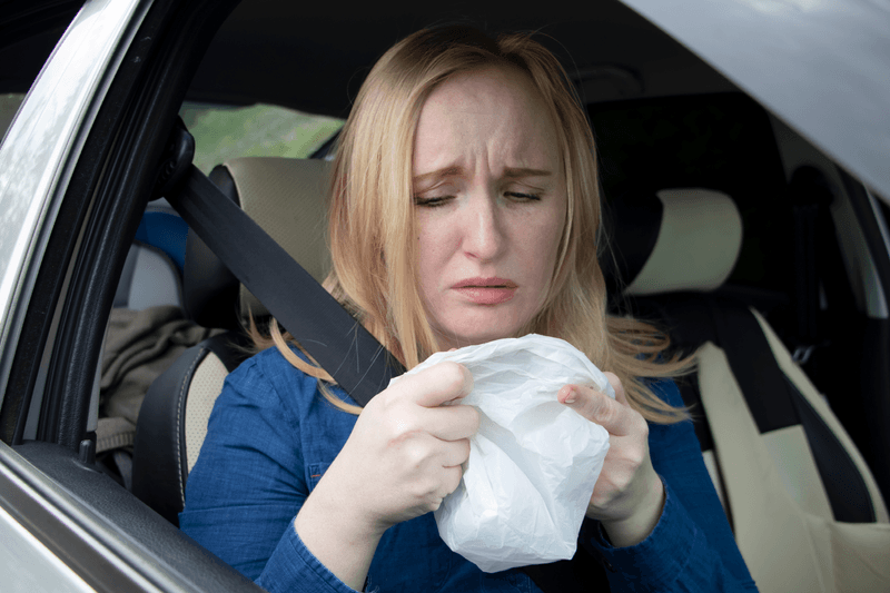 Person in a car, holding a white plastic bag, looking nauseous