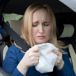 Person in a car, holding a white plastic bag, looking nauseous
