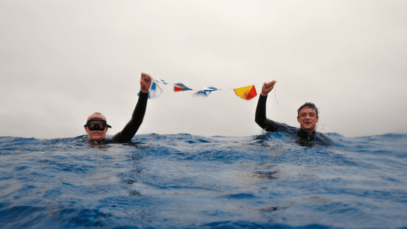 chris and mika brown in the sea holding up maritime flags that spell "nemo" at point nemo