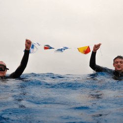 chris and mika brown in the sea holding up maritime flags that spell "nemo" at point nemo
