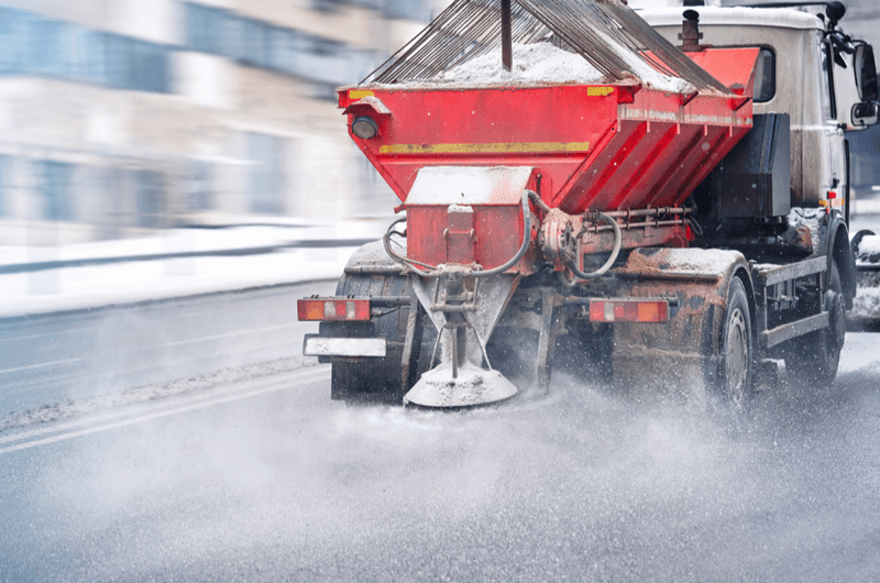 Road and highway maintenance gritter truck spreading de-icing salt on road in winter. Salt spreading. Snow plow service truck removing snow and spreading salt on snowy city road during blizzard