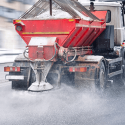 Road and highway maintenance gritter truck spreading de-icing salt on road in winter. Salt spreading. Snow plow service truck removing snow and spreading salt on snowy city road during blizzard